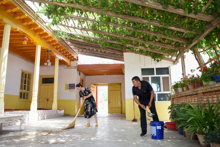 在新疆喀什地区疏附县阿亚格曼干村,村民阿卜都克尤木·肉孜(右)和妻子在打扫庭院(2022年6月10日摄)。新华社记者 丁磊 摄